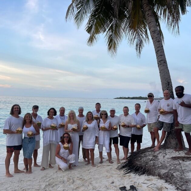 A joyful group of people sipping coconut water by the beach - Maldives SUP surf trip with Tiago Silva - Live Aboard Surfing - Zhoola