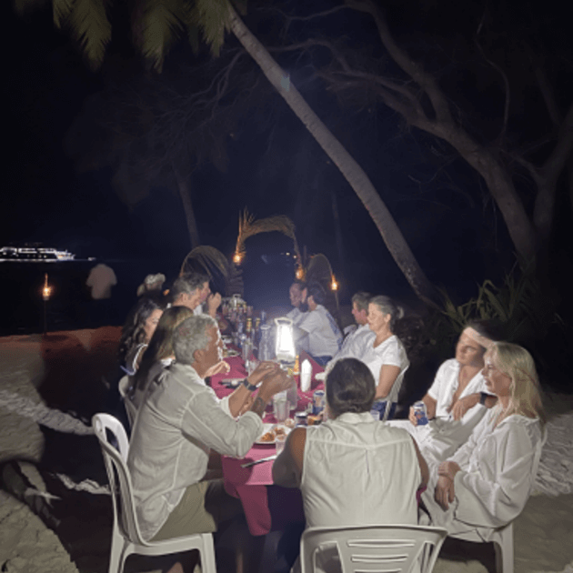 Load image into Gallery viewer, A group of surfers gathered around a round table, enjoying a dinner together after a day of surfing - -Maldives SUP surf trip with Tiago Silva - Live Aboard Surfing - Zhoola
