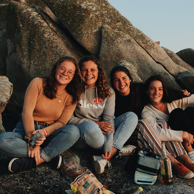 Load image into Gallery viewer, Group of cheerful, diverse girls of different backgrounds sitting together on a rockside.Tranquility and natural splendor with Nateea - Yoga and Safari - RETREAT - Zhoola
